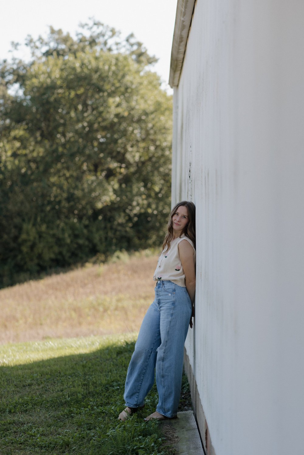 Ariel standing against a white barn wall in jeans and a cream top